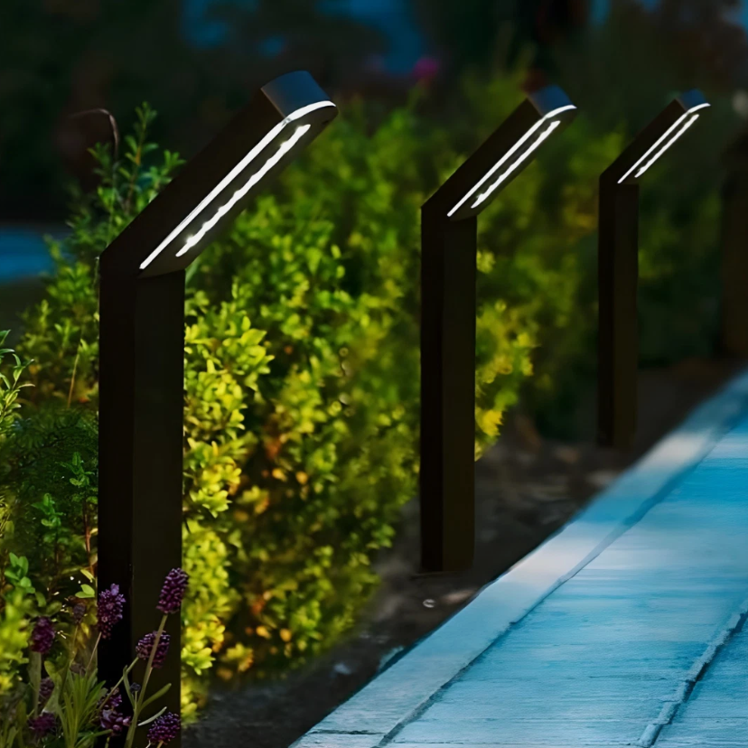 Three black outdoor solar lights on a wooden deck with greenery in the background