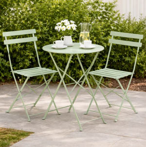 Light green metal outdoor table and chairs with a small plant and cups on a patio.