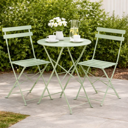 Light green metal outdoor table and chairs with a small plant and cups on a patio.
