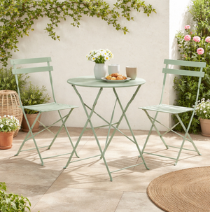 Green metal outdoor table and chairs set with plants and a basket on a patio.