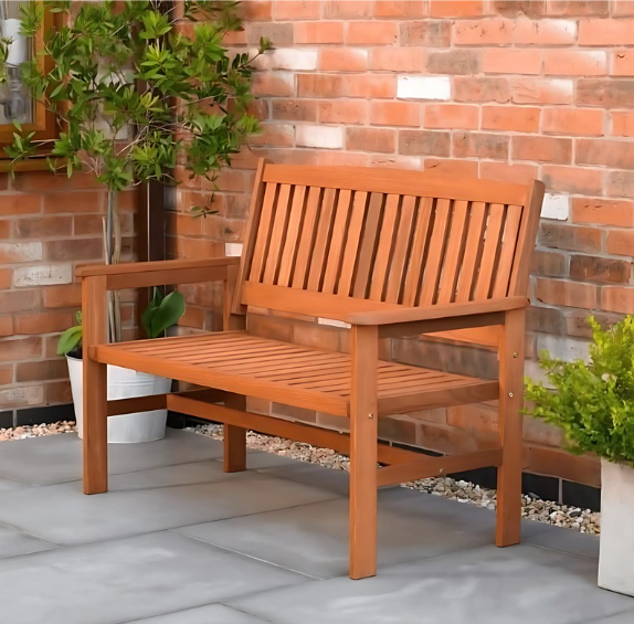 Wooden bench on a patio with a brick wall and plants in the background