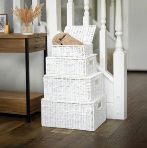 Stack of white wicker baskets on a wooden floor with a staircase in the background.