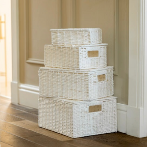 Stack of white wicker baskets on a wooden floor with a neutral wall background