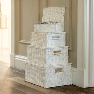 Stack of white wicker storage baskets on a wooden floor.