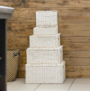Stack of white wicker baskets against a wooden wall.