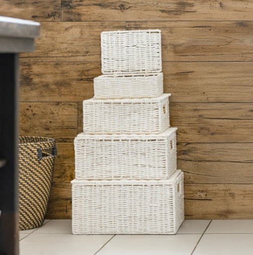 Stack of white wicker baskets against a wooden wall.
