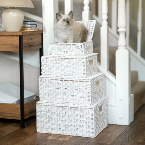 Stack of white wicker baskets with a cat sitting on top in a home setting.