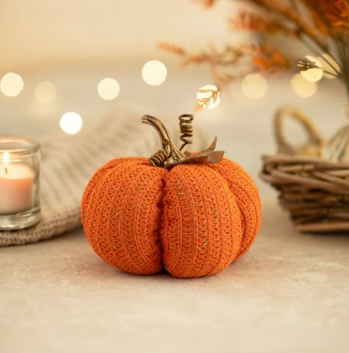 Knitted pumpkin decoration on a table with blurred lights and basket in the background