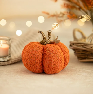Knitted pumpkin decoration on a table with blurred lights and basket in the background