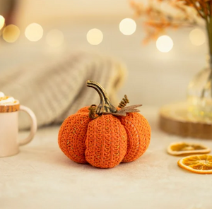 Knitted pumpkin decoration on a table with blurred lights and oranges in the background