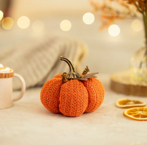 Knitted pumpkin decoration on a table with blurred lights and oranges in the background