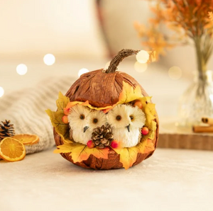 Decorative pumpkin with owl figurines and autumn leaves on a soft surface.