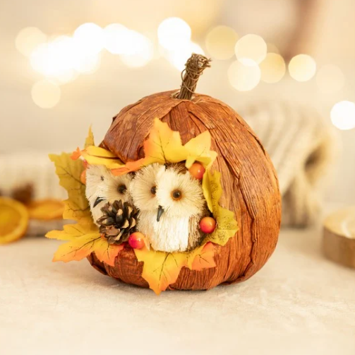 Decorative pumpkin with a small owl figurine and autumn leaves on a blurred background