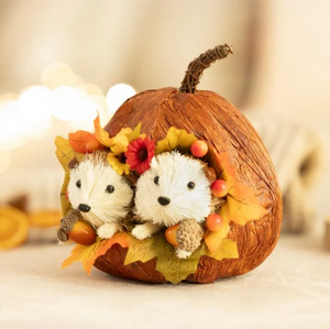 Decorative pumpkin with hedgehog figurines and autumn leaves on a blurred background
