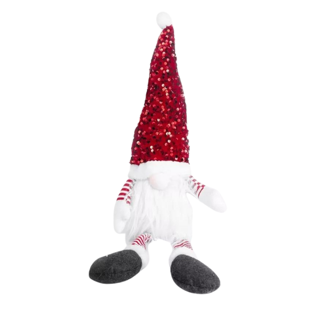 A plush Christmas gonk decoration with a red hat, white beard, and striped gloves, seated on a box with a Christmas tree in the background.