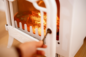 Hand using a tool to adjust the glowing interior of a white electric stove.