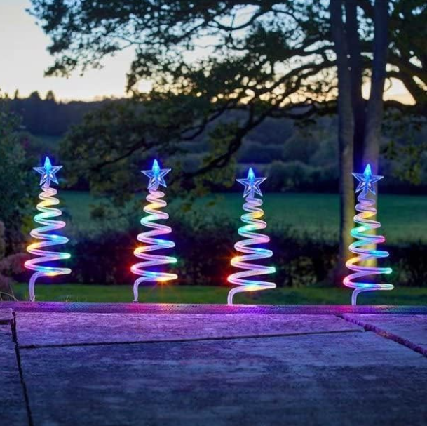 Four colorful spiral light trees on a patio with a garden and tree in the background.