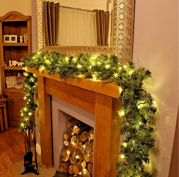 Decorative fireplace with green garland and lights, surrounded by wooden furniture and a mirror.