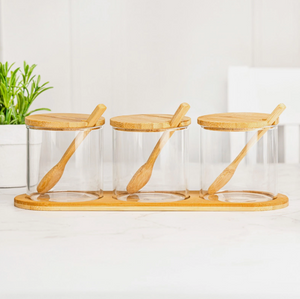 Three glass jars with wooden lids and spoons on a wooden stand against a white background.