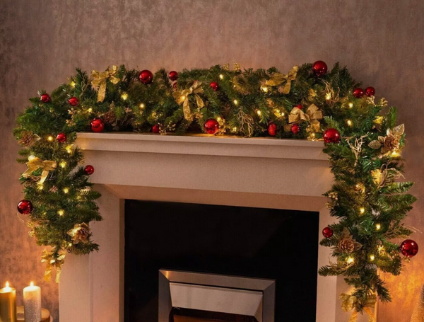 Christmas wreath with a gold bow and red ornaments on a warm-toned background.