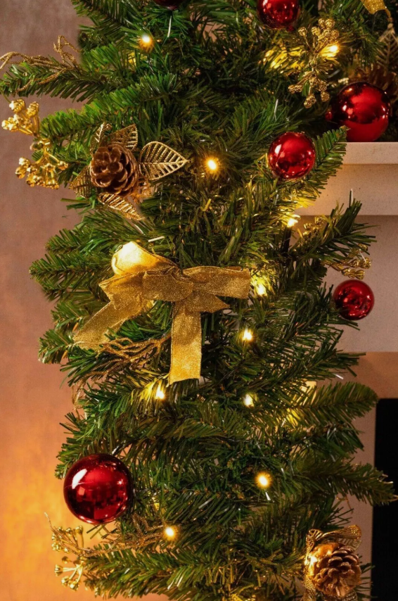 Christmas wreath with a gold bow and red ornaments on a warm-toned background.