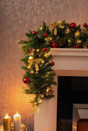 Christmas wreath with a gold bow and red ornaments on a warm-toned background.