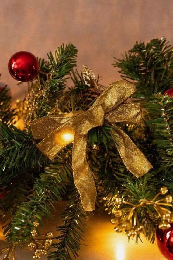 Close-up of a Christmas wreath with a gold bow and red ornaments on a warm-toned background.