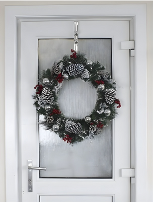 Decorative Christmas wreath with pinecones and red berries hanging on a glass door.