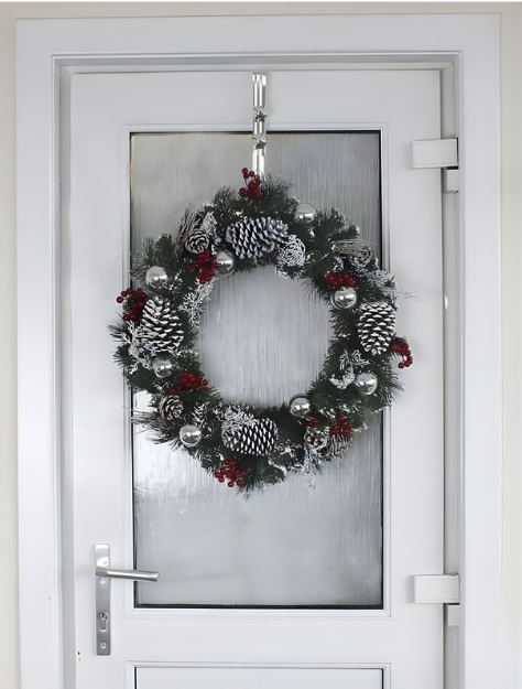 Decorative Christmas wreath with pinecones and red berries hanging on a glass door.