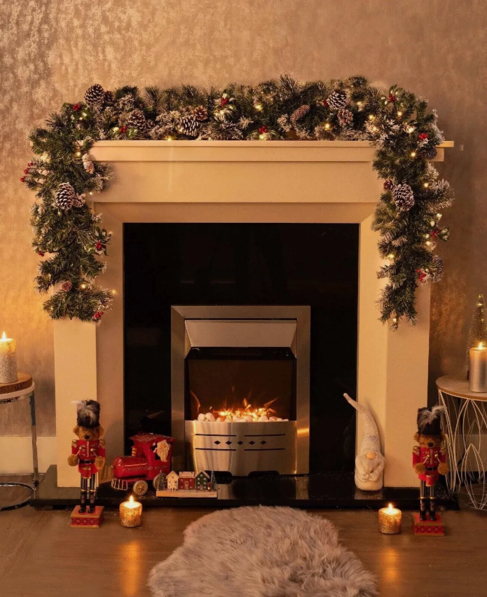 Decorated fireplace with Christmas garland, candles, and small figures in a cozy room.