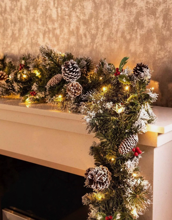 Decorative Christmas garland with lights on a mantelpiece against a gold textured wall.