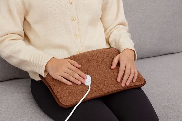 Person holding a brown heating pad on a gray couch