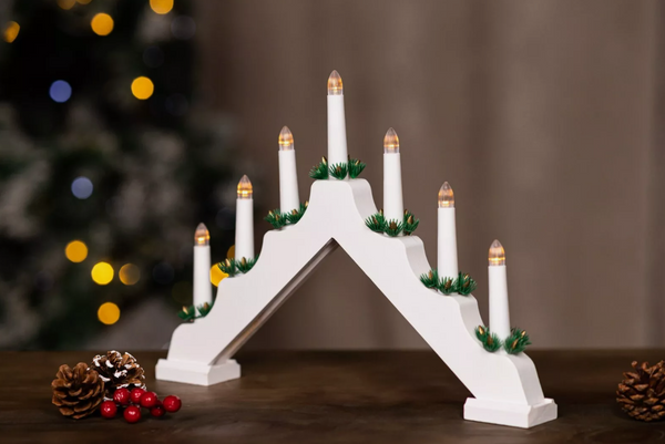 Decorative white arch with candles in front of a blurred Christmas tree with lights.