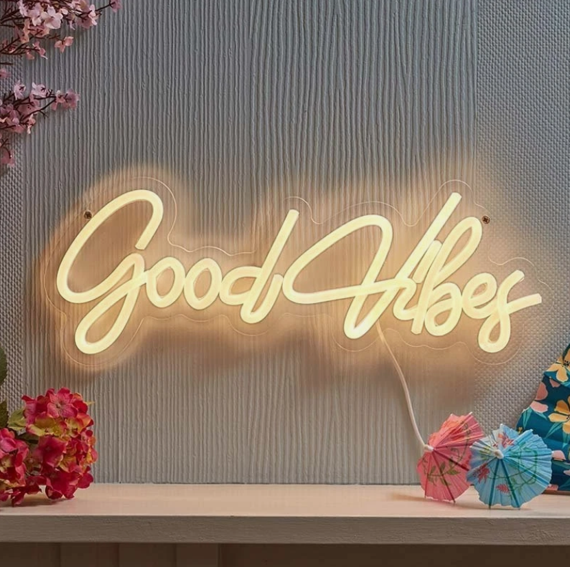 Neon sign with 'Good Vibes' on a textured wall with flowers and decorative items.