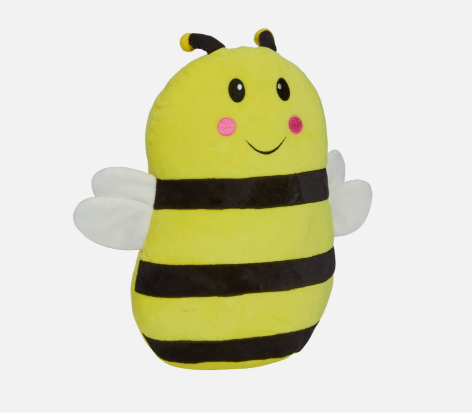 Plush bee-shaped pillow on a bed with a lamp in the background