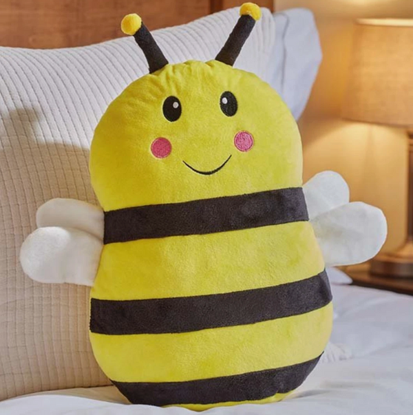 Plush bee-shaped pillow on a bed with a lamp in the background