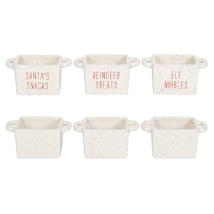 Six small rectangular ceramic containers with side handles, arranged in two rows of three on a white background. The top row is labeled 'SANTA'S SNACKS', 'REINDEER TREATS', and 'ELF NIBBLES' in coral-red text, while the bottom row is empty.
