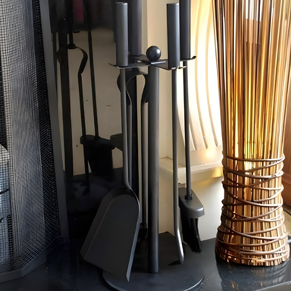 Set of fireplace tools including a poker, brush, and tongs on a stand next to a decorative vase.