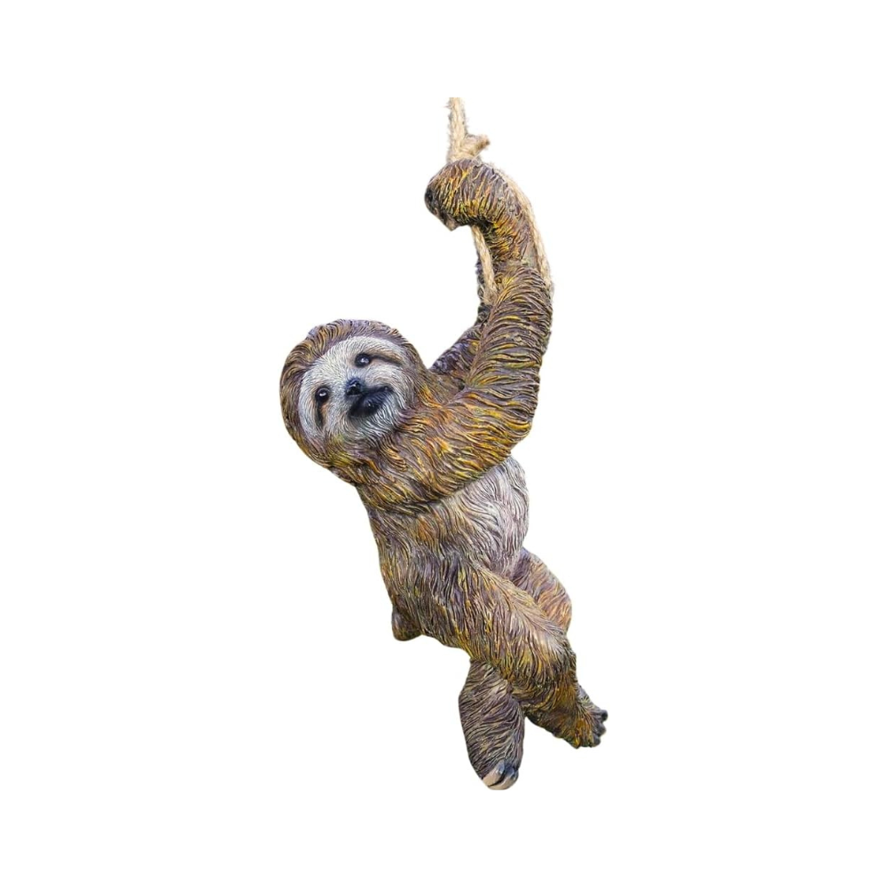 A realistic sloth hanging ornament or decoration is suspended from a tree branch in a sunny backyard garden with green grass, bushes, and flowers.
