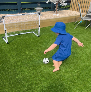 Child playing with a soccer ball near a small goalpost on grass