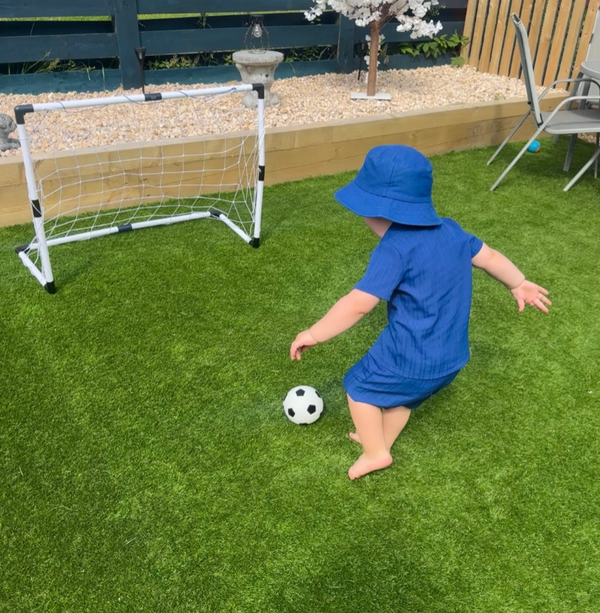 Child playing with a soccer ball near a small goalpost on grass