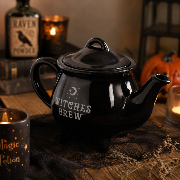 Glossy black Witches Brew ceramic teapot with crescent moon design, styled on a wooden table with Halloween décor.