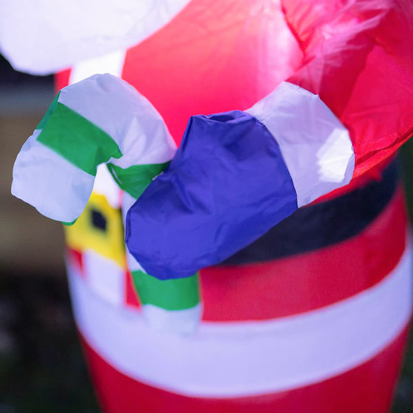 A close-up of a red, white, and blue inflatable Santa Claus body with a green and white striped scarf, photographed outdoors with a blurred background.