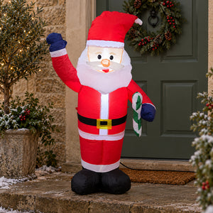 Inflatable Santa Claus holiday decoration standing on a stone doorstep in front of a green door with a wreath. The Santa figure wears a red suit with white trim, a black belt, blue gloves, black boots, and holds a candy cane.