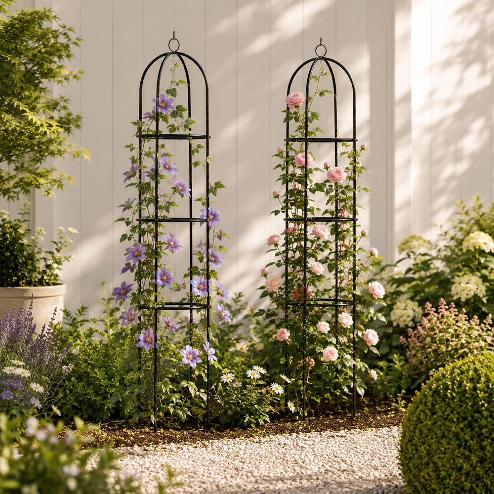 Two black metal arched garden trellises with climbing flowers, shown in a landscaped garden setting against a white fence.