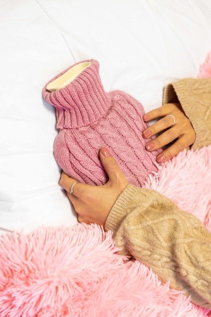 Person holding a pink knitted hot water bottle against a white background