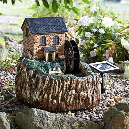 Decorative water fountain with a small house and wheel in a garden setting