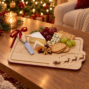 A wooden Christmas charcuterie board with engraved reindeer and 'Merry Christmas' text, styled with cheese, crackers, grapes, and a knife on a wooden table in a cozy holiday living room setting.