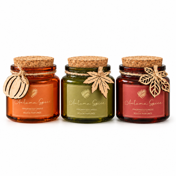 Three small glass jar candles with cork lids are arranged side by side on a white background. The left jar is amber-orange, the middle is olive green, and the right is muted red.