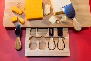 Wooden cutting board with cheese and four cheese knives on a red background